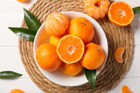 Bowl with sweet mandarins and leaves on white wooden background