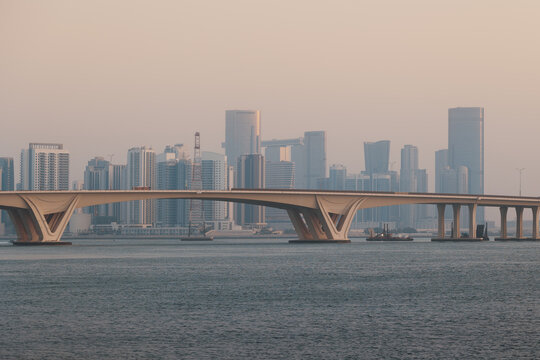 Big modern city on sea shore many skyscrapers concrete bridge in golden sunrise glow, Abu Dhabi, UAE