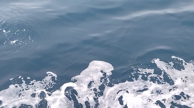 Sea water foams under a moving ship, which is moving away in the opposite direction