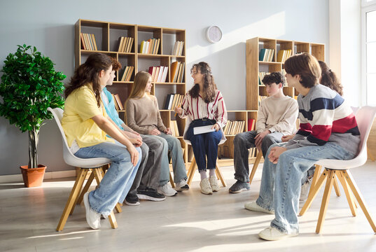 Students teenagers with teacher counselor in discussion circle. Teens in a sunlit library classroom share group experiences, building empathy and skills. Concept youth support and education.