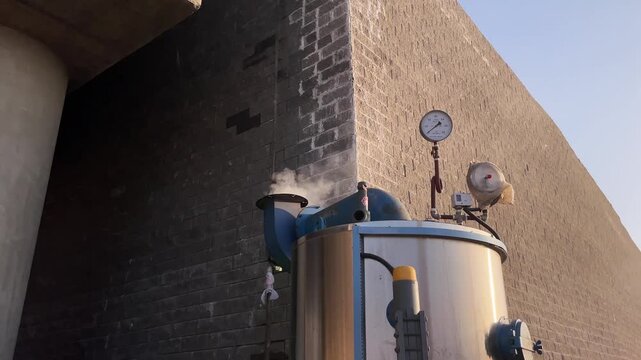 Industrial boiler releasing steam next to a concrete wall