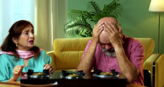 A worried retired Indian Asian couple showing stress because of no cooking gas cylinder inside their home kitchen because of a sudden LPG shortage and lack of fuel supply for preparing meals.