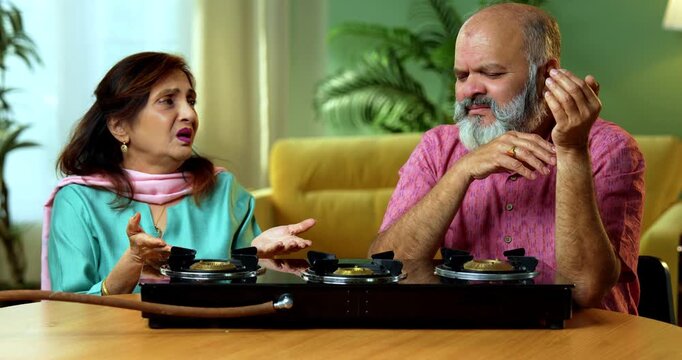 A worried retired Indian Asian couple showing stress because of no cooking gas cylinder inside their home kitchen because of a sudden LPG shortage and lack of fuel supply for preparing meals.