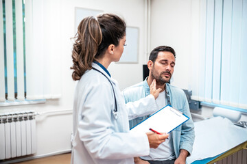 Fototapeta premium Professional female doctor checking a male patient's lymph nodes by palpating his neck. Healthcare worker with a clipboard performing a physical exam. Medical consultation and diagnosis concept.