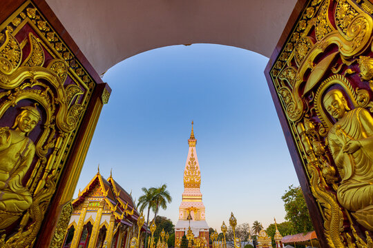 Golden Pagoda of Wat Phra That Phanom through Ornate Temple Doorway at Twilight, Nakhon Phanom, Thailand,A stunning wide-angle view of the iconic Phra That Phanom pagoda, a sacred Buddhist landmark.