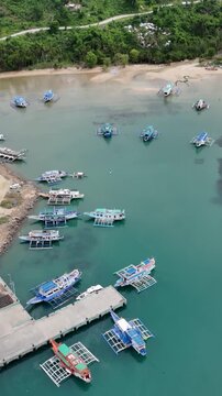 Aerial drone view of colorful traditional banca boats docked near a small pier in Dapa Port, Siargao, Philippine. Vertical