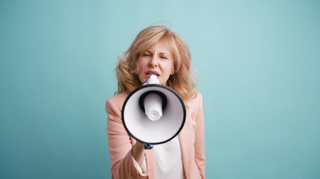 Upset senior businesswoman yelling into a megaphone. Angry female activist protesting and making an announcement against a blue background