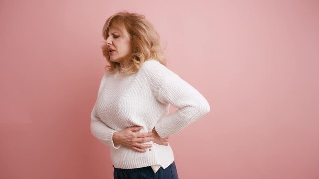 Elderly woman experiencing sudden lower back pain and discomfort. Unhealthy senior person feeling muscle aches and touching her spine