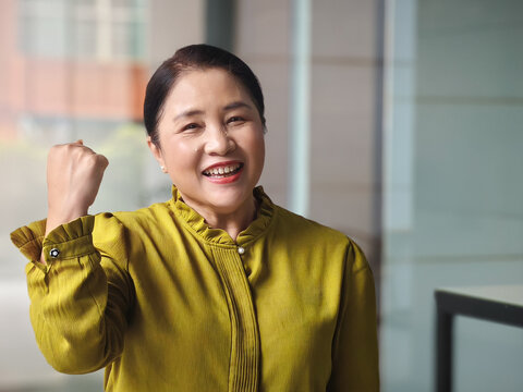 Healthy and strong smiling old senior asian woman in her 50s showing positive satisfying face expression in healthy green urban environment, image concept for old age success and healthy lifestyle
