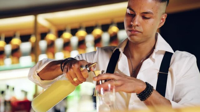 Concentrated barman carefully pouring yellow liquor from a bottle into a jigger to measure ingredients for a mixed drink at a bar