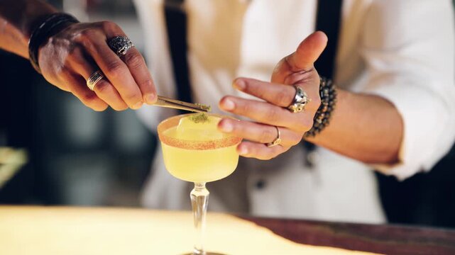 Close up view of a skilled mixologist's hands carefully adding the final touch to a craft cocktail with tweezers in a speakeasy bar