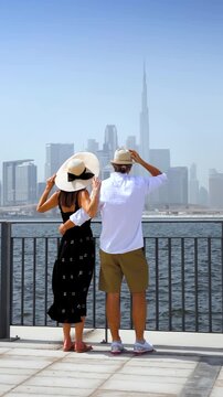 A beautiful tourist couple on a sightseeing trip enjoys the view of the skyline of Dubai, UAE, as a city travel concept