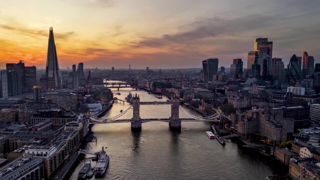 Aerial hyperlapse sunset view of the illuminated Tower Bridge and City skyline of London, UK, with river and street traffic
