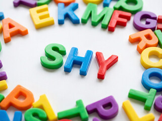 Fototapeta premium Bright plastic letters spell SHY in center. Colorful letters surround the word in a circle. White background highlights the bold, playful text