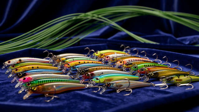Multicolored hard plastic fishing lures featuring realistic scale patterns and sharp metal treble hooks are arranged in a group to showcase their vibrant reflective finishes and specialized...