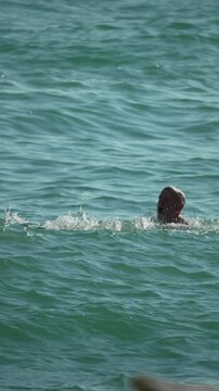 Man, ocean, flip, an active person performs a somersault in the clear blue sea. Vertical video.