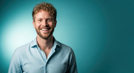 Fototapeta premium Smiling young man in light blue shirt on teal background