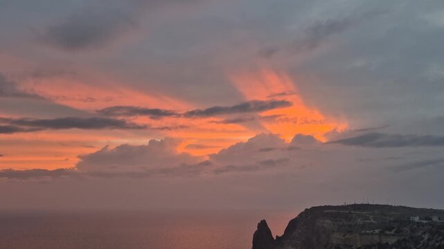Sunset ocean cliffs dramatic red and orange sunrays piercing through dark clouds over coastal rock formation landscape