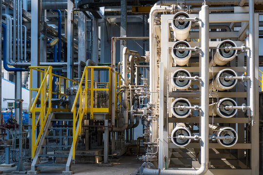 A wide shot of a complex industrial water treatment facility. The image features multiple white reverse osmosis membrane pressure vessels arranged in a rack, connected by a network of stainless steel 