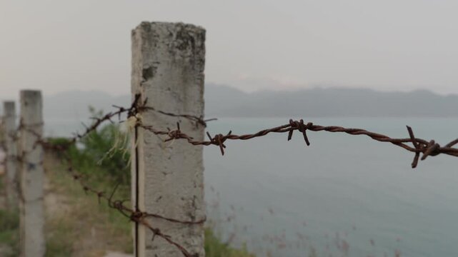 Rusty Barbed Wire Fence on Concrete Posts Overlooking Coastal Border Zone