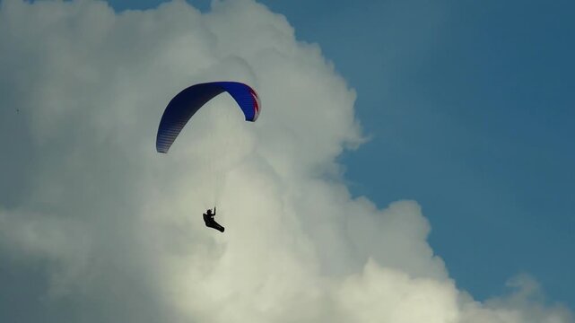 Paraglider gently floats in the sky against a background of beautiful clouds summer day.