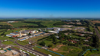 Fototapeta premium An aerial view of a large industrial complex surrounded by green fields and trees under a clear blue sky
