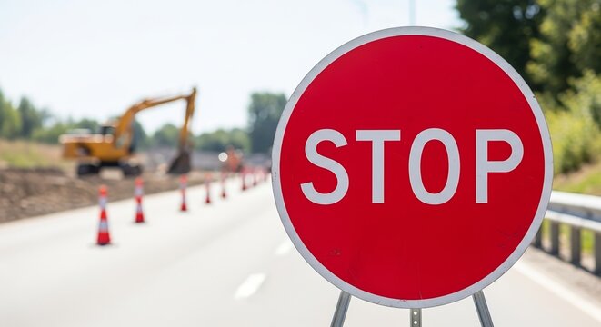 Temporary stop sign on pole in front of construction zone and roadworks with machinery and traffic cones. Stop sign alerts drivers about road developments and necessary caution.