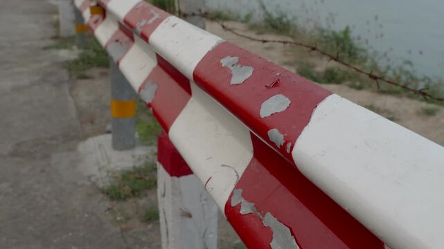 Weathered red and white striped crash barrier with chipped paint, neglected public infrastructure