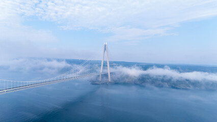 Fototapeta premium Aerial view of Yavuz Sultan Selim Bridge in Istanbul above clouds. Modern bridge pylon through white fog. Ethereal Bosphorus landscape at Poyrazkoy. Atmospheric drone photography.