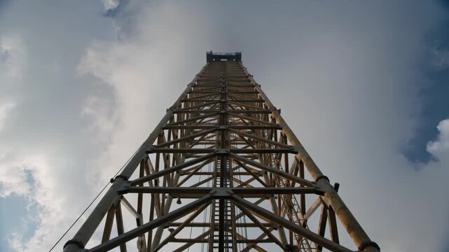 Vertical steel lattice tower reaches toward moving clouds to represent global connectivity and industrial infrastructure growth.