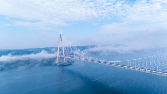 Aerial view of Yavuz Sultan Selim Bridge in Istanbul above clouds. Modern suspension bridge pylon through white fog. Ethereal Bosphorus landscape at Poyrazkoy. Atmospheric drone photography.