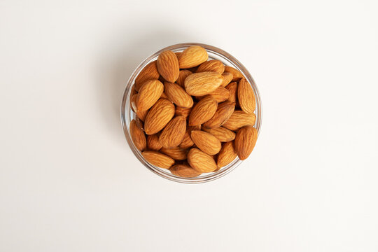 glass bowl filled with almonds on a neutral background, framed more tightly to emphasize shape
