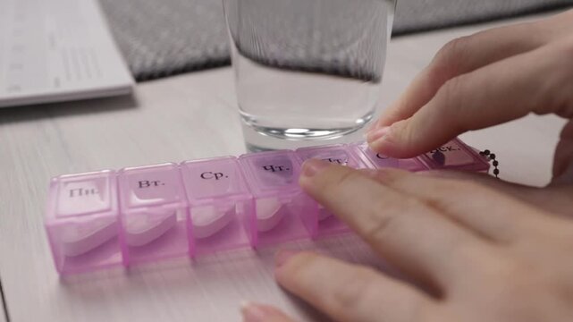 hands open pill organizer compartments, preparing weekly medication doses and adherence routine