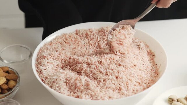 hands stirring uncooked rice tinted with spice mixture in a shallow bowl, showing texture color and seasoning before the grains go into the pot