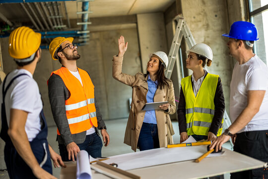 Female engineer pointing at ceiling pipes and explaining installation details to her construction team.