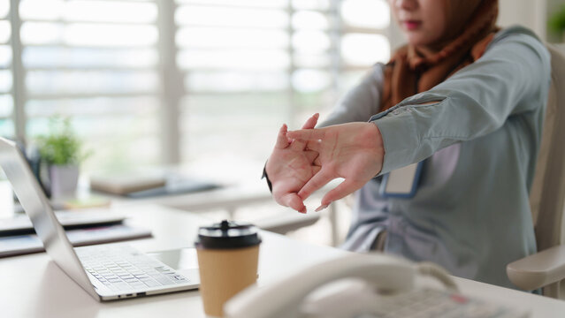 Asian adult woman taking work break stretching hands at modern office desk preventing fatigue maintaining health wellness during remote work productivity 