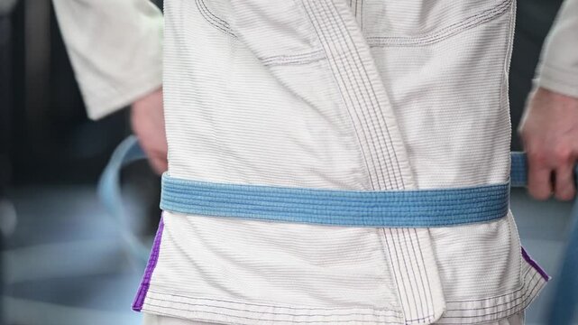 Martial arts tying kimono Gi jiujitsu karate blue belt, traditional, belt, blurred out background video, selective focus cinematic, gym setting