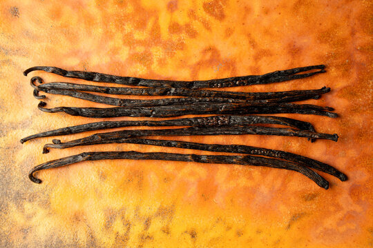 Whole vanilla beans on an orange surface 