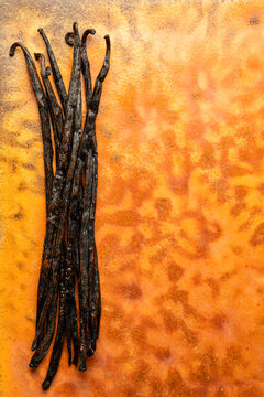 Whole vanilla beans on an orange surface 