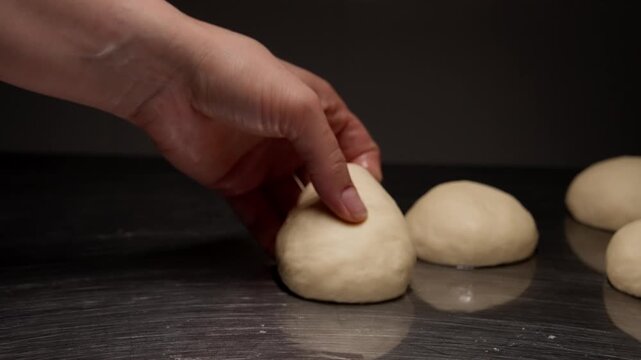 Close-up sequence of freshly kneaded dough balls resting on a reflective metal surface while a baker hand gently shapes and prepares each portion for baking