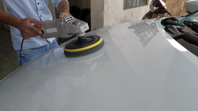 Close-up of a person polishing a car surface using an electric buffer machine. Automotive detailing process to restore shine and remove scratches, concept of car care, maintenance, and professional cl