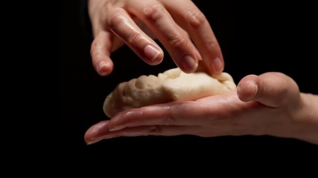 Closeup hands shaping delicate dough dumpling with careful pleating technique against dark background, highlighting craftsmanship, texture, and culinary artistry