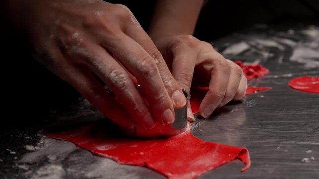 Close-up sequence of hands using a round metal cutter to shape bright red dough circles on a floured work surface in a professional baking environment