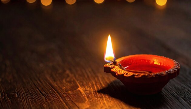 Traditional clay diya lamp glowing on dark wooden background