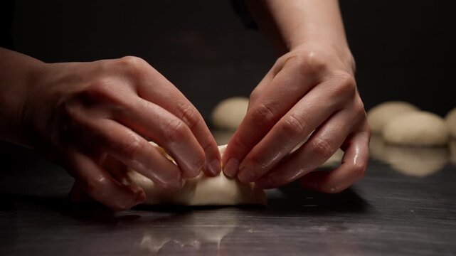 Close up of skilled hands carefully folding and shaping delicate dough dumplings on a reflective metal surface in a dark kitchen setting, emphasizing craft and texture