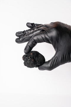 Trufa negra en mano con guante negro sobre fondo blanco