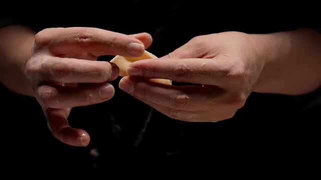 Closeup of skilled hands carefully folding and sealing a small dumpling wrapper around the filling, showcasing delicate homemade cooking technique against dark background