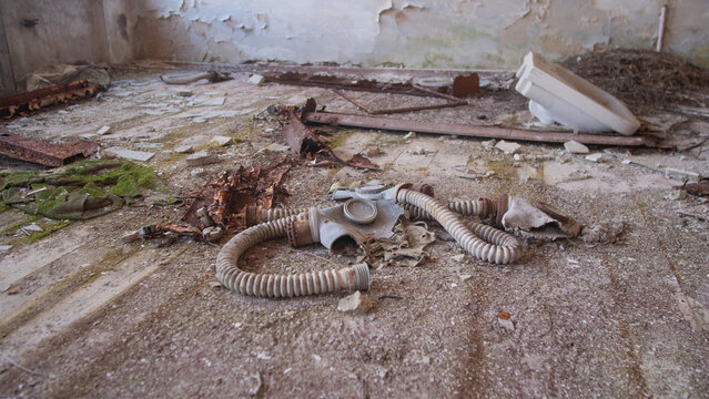 Gas Mask Abandoned On Cracked Floor, Discarded Decontamination Gear With Coiled Hoses, Peeling Plaster, Moss