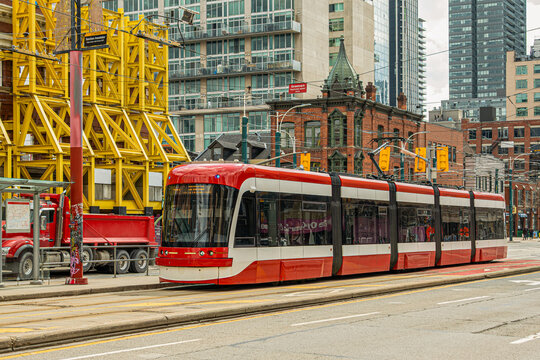 Red modern Toronto  streetcar  passing Victorian-era heritage commercial building  and construction site amid modern downtown towers.