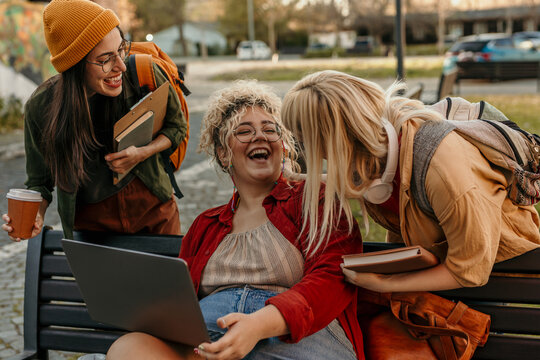 Diverse students laughing and collaborating on campus using laptop